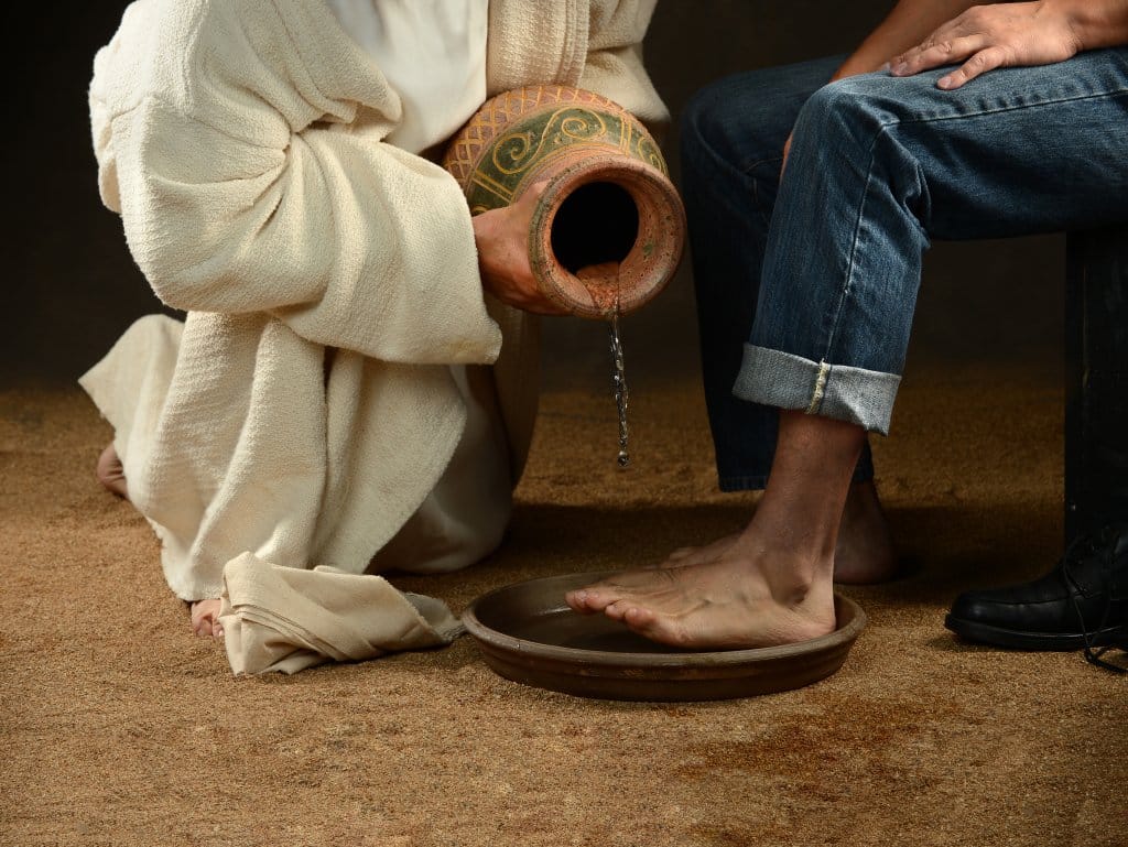 Jesus pouring water to wash feet of modern man over dark background